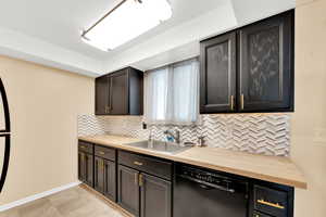 Kitchen with butcher block counters, black dishwasher, and decorative backsplash