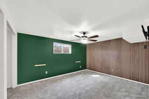 Unfurnished bedroom featuring a textured ceiling, carpet, an accent wall, wooden walls, and ceiling fan
