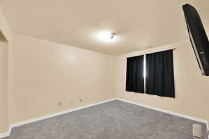 Carpeted spare room featuring a textured ceiling and baseboards