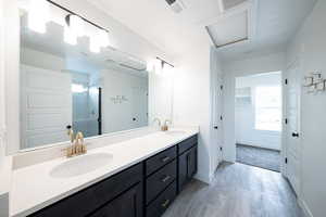 Bathroom with double vanity, a shower stall, light wood-type flooring, and a walk in closet
