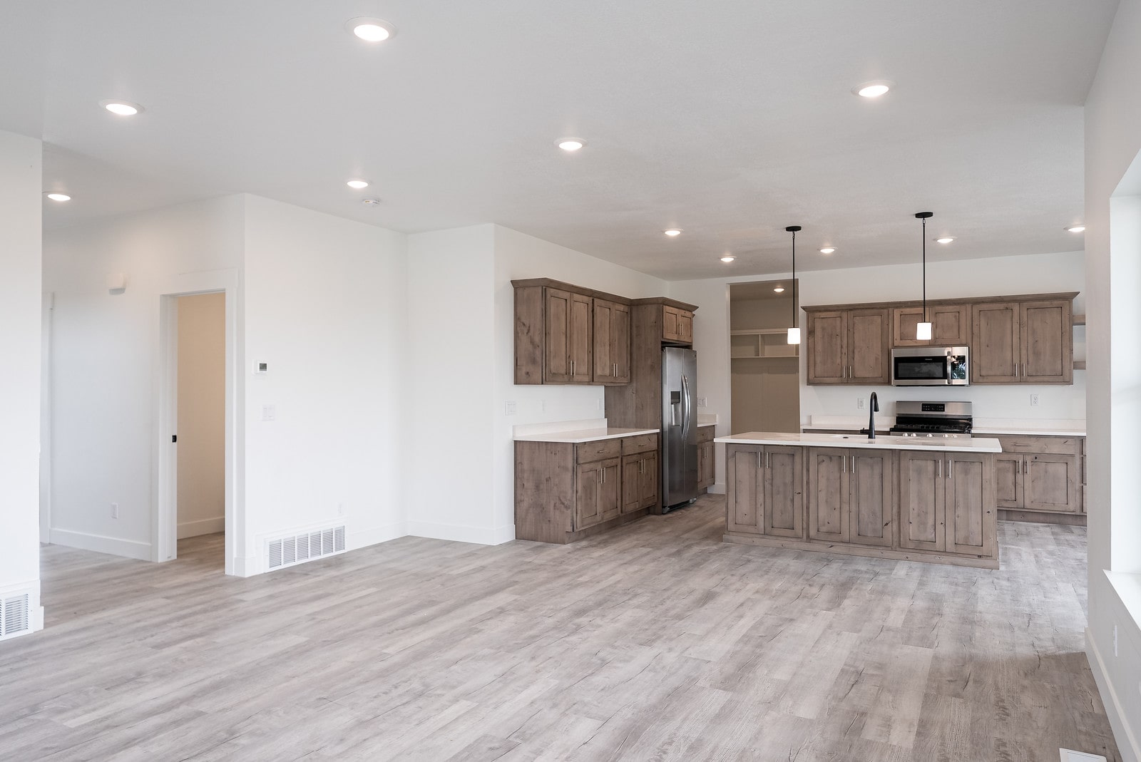 Kitchen with stainless steel appliances, pendant lighting, light wood-style flooring, an island with sink, and open floor plan