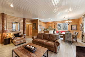 Living area with hanging lights, log walls, light wood-type flooring, and wood ceiling