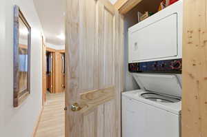 Laundry area with stacked washer and dryer and light wood-style flooring