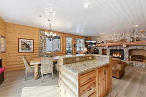Kitchen with hanging lights, light wood finish cabinetry, a stone fireplace, a kitchen island, and light stone countertops