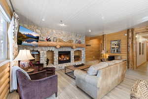 Living area with log walls, a fireplace, light wood finished floors, wooden ceiling, and plenty of natural light