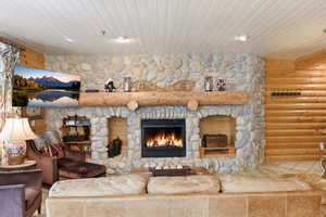 Living room with wooden ceiling, a stone fireplace, and log walls