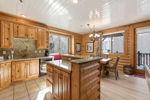 Kitchen with a kitchen island, suspended lighting, log walls, dishwasher, and light stone countertops