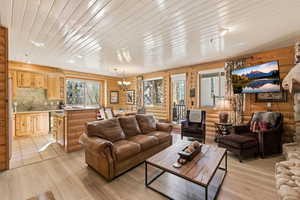Living room featuring hanging lights, light wood-style floors, log walls, and wooden ceiling