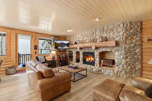 Living area with wood ceiling, a stone fireplace, rustic walls, wood finished floors, and wooden walls