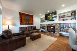 Living room featuring wood finished floors, built in shelves, a stone fireplace, and recessed lighting