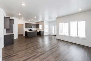 Kitchen with open floor plan, a center island, dark wood finish cabinets, light countertops, and dark wood-style floors