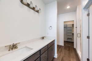 Bathroom featuring double vanity, a walk in closet, dark wood-type flooring, and a stall shower