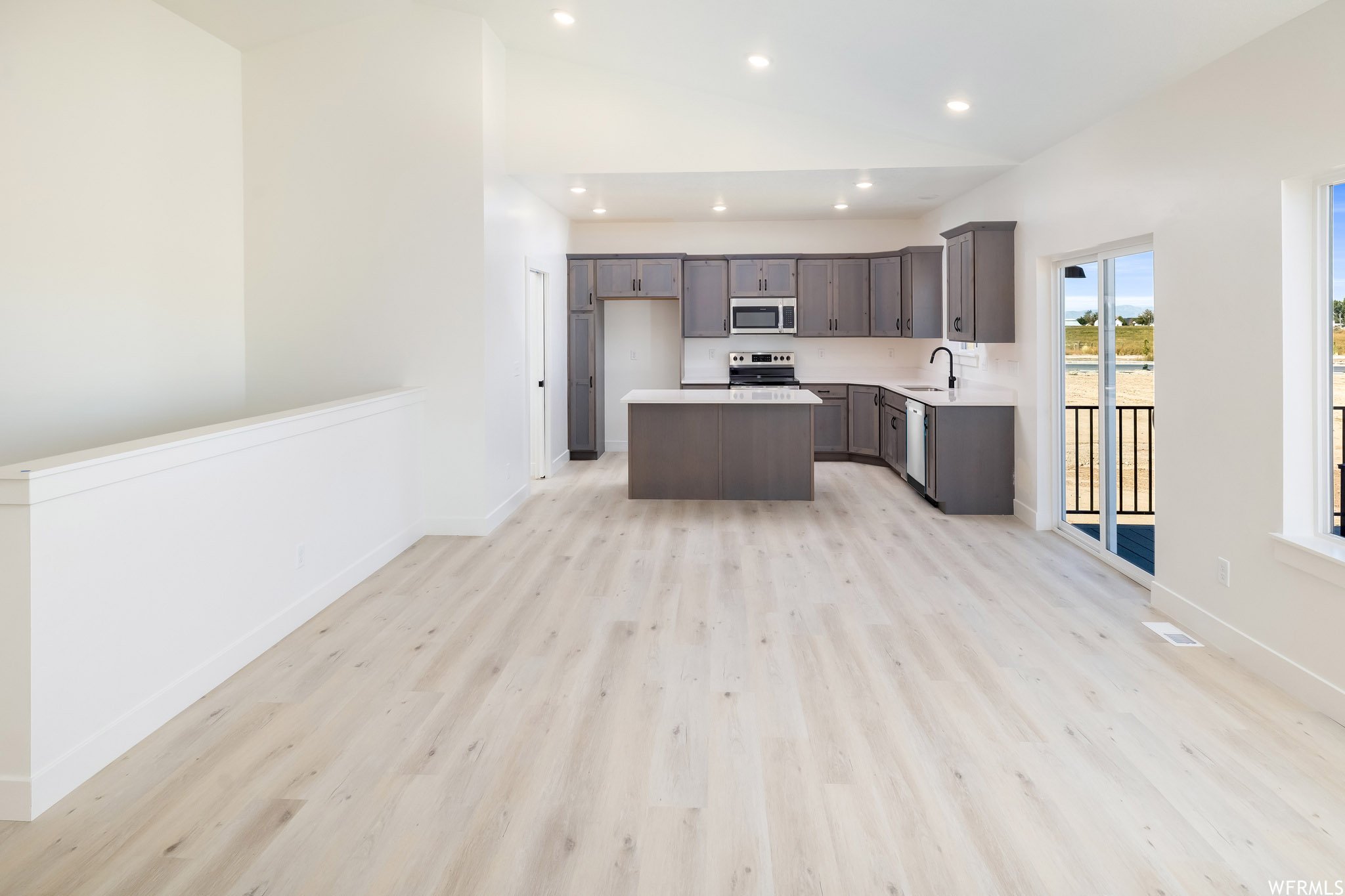 Kitchen featuring open floor plan, a kitchen island, light countertops, lofted ceiling, and light wood-style flooring