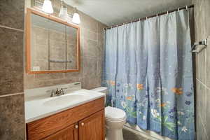Full bathroom with tile walls, vanity, and a textured ceiling