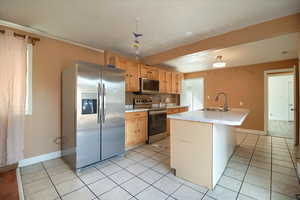 Kitchen with stainless steel appliances, a kitchen island with sink, light countertops, light wood finish cabinets, and a kitchen bar