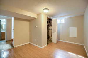 Unfurnished bedroom featuring ensuite bathroom, a textured ceiling, light wood-style flooring, gas water heater, and a closet