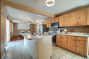 Kitchen with stainless steel appliances, an island with sink, light countertops, light tile patterned floors, and decorative backsplash
