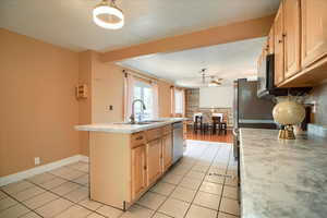 Kitchen featuring a center island with sink, light wood finish cabinets, light countertops, light tile patterned floors, and stainless steel appliances