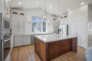 Kitchen with vaulted ceiling, a kitchen island, dual tone cabinets, glass fronted cabinets, and stainless steel appliances