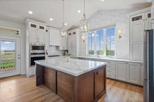 Gourmet kitchen featuring a substantial central island with a solid surface countertop, white shaker cabinetry, stainless steel appliances, and wood-finish flooring