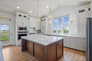 Two tone kitchen with glass fronted cabinets, lofted ceiling, a center island, stainless steel appliances, and two tone cabinets