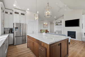 Kitchen with stainless steel refrigerator with ice dispenser, built in shelves, a kitchen island, two tone cabinetry, and light stone counters