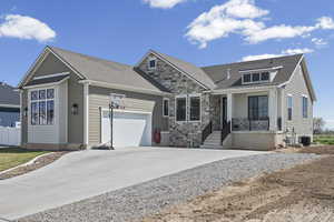 View of front facade featuring a shingled roof, an attached garage, concrete driveway, stone siding, and covered porch