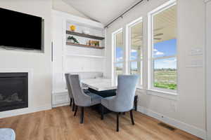 Dining space featuring light wood-type flooring, a glass covered fireplace, vaulted ceiling, and built in shelves