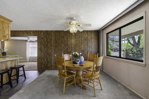 Dining room featuring a ceiling fan, a textured ceiling, carpets and LVP flooring, and wood panel walls
