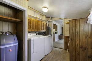 Laundry and pantry area with wooden walls, light wood-style floors, wainscoting, separate washer and dryer, and water heater