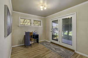 Doorway to outside with wood finished floors and crown molding