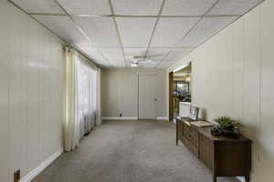 Unfurnished room featuring a drop ceiling, wooden panel walls, light colored carpet, and a ceiling fan