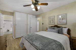 Bedroom featuring a textured ceiling, light wood finished floors, two closets, ceiling fan, and wallpapered walls