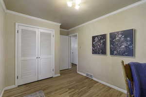Unfurnished bedroom featuring light wood-style flooring, a closet, and crown molding