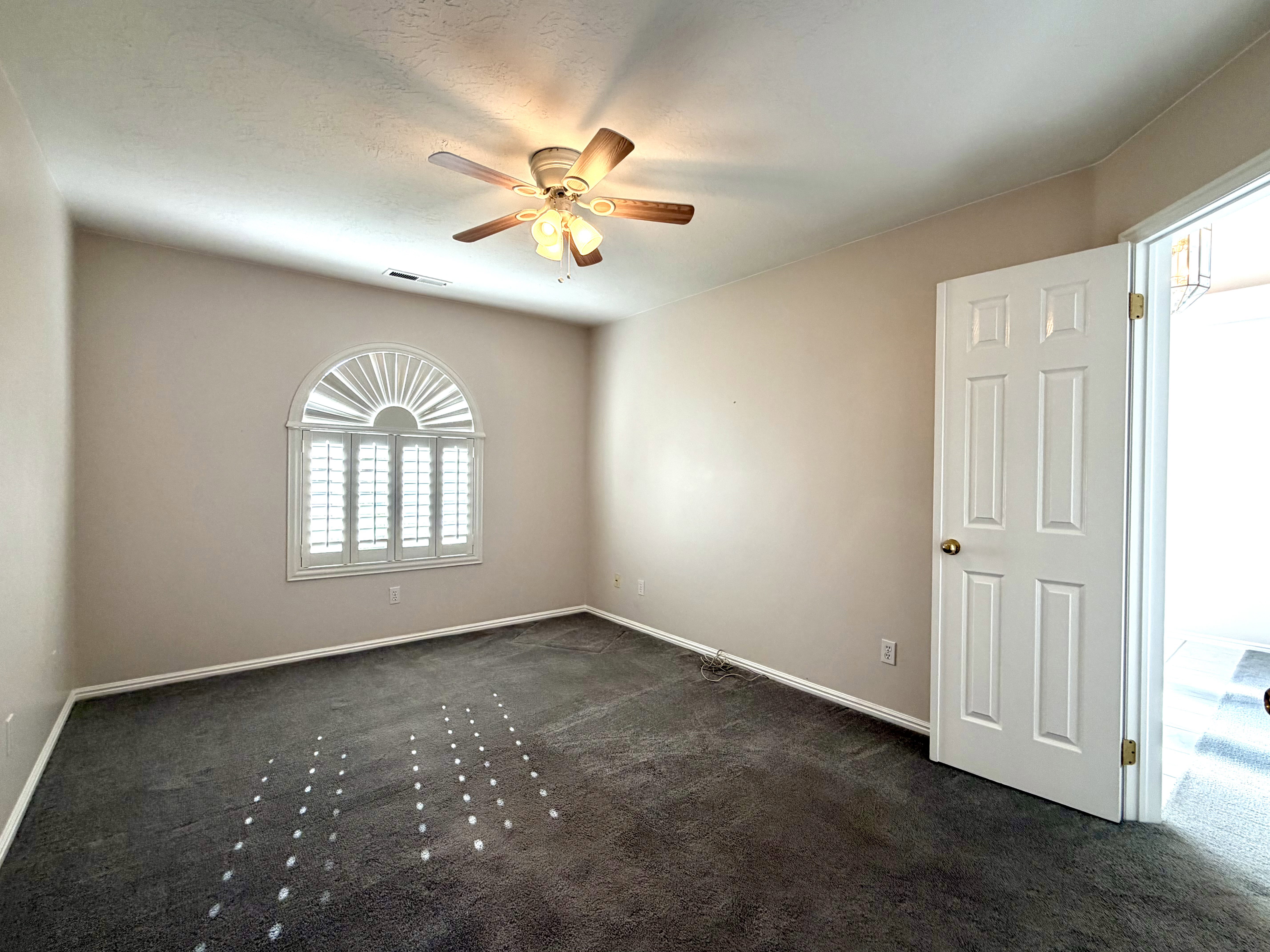 Neutral-toned room with plush carpeting and a decorative arched window featuring white plantation shutters