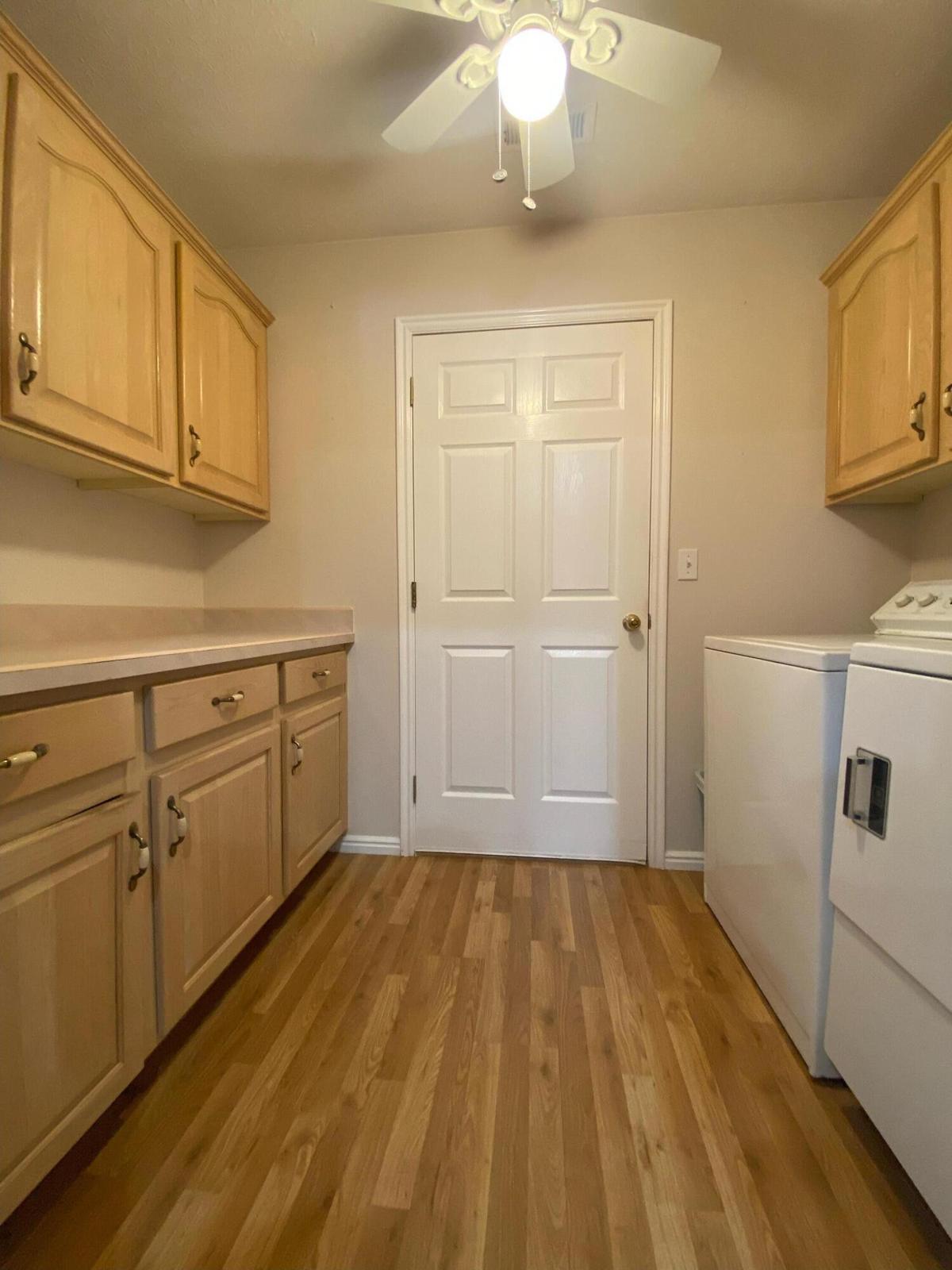 Utility space featuring wood-finish flooring, light wood cabinetry with brass hardware, and a white paneled door