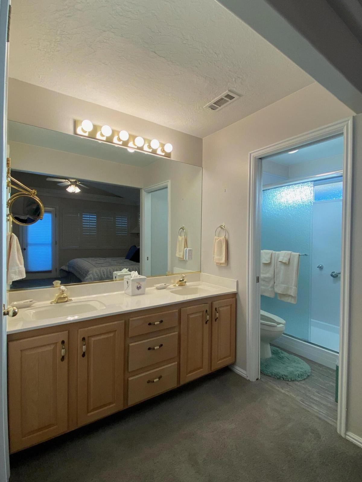 Double vanity featuring light wood-finish cabinetry, dual sinks, and a large wall-mounted mirror