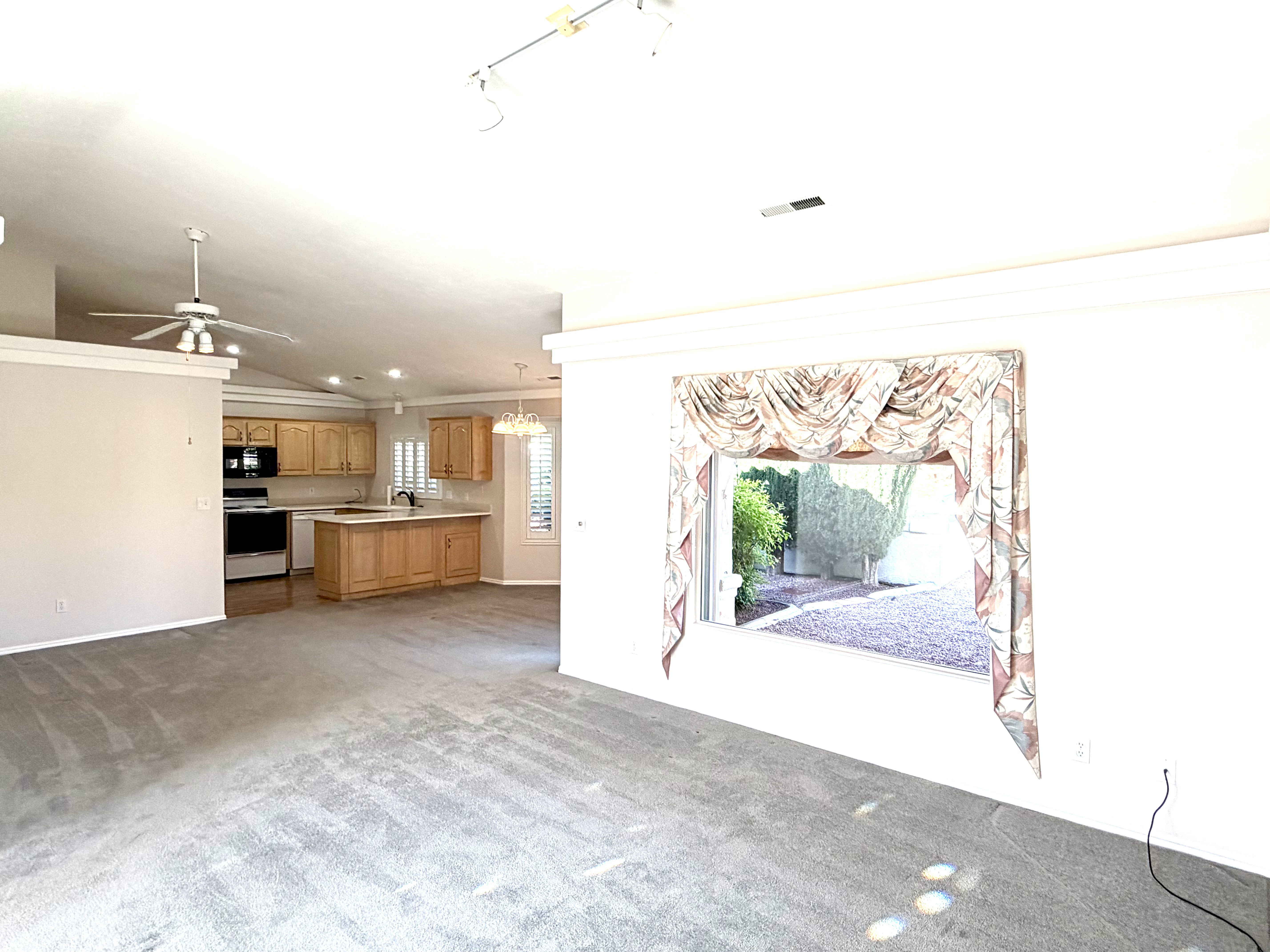 Open-concept living space featuring vaulted ceilings, carpet flooring, and a kitchen with wood cabinetry and an island
