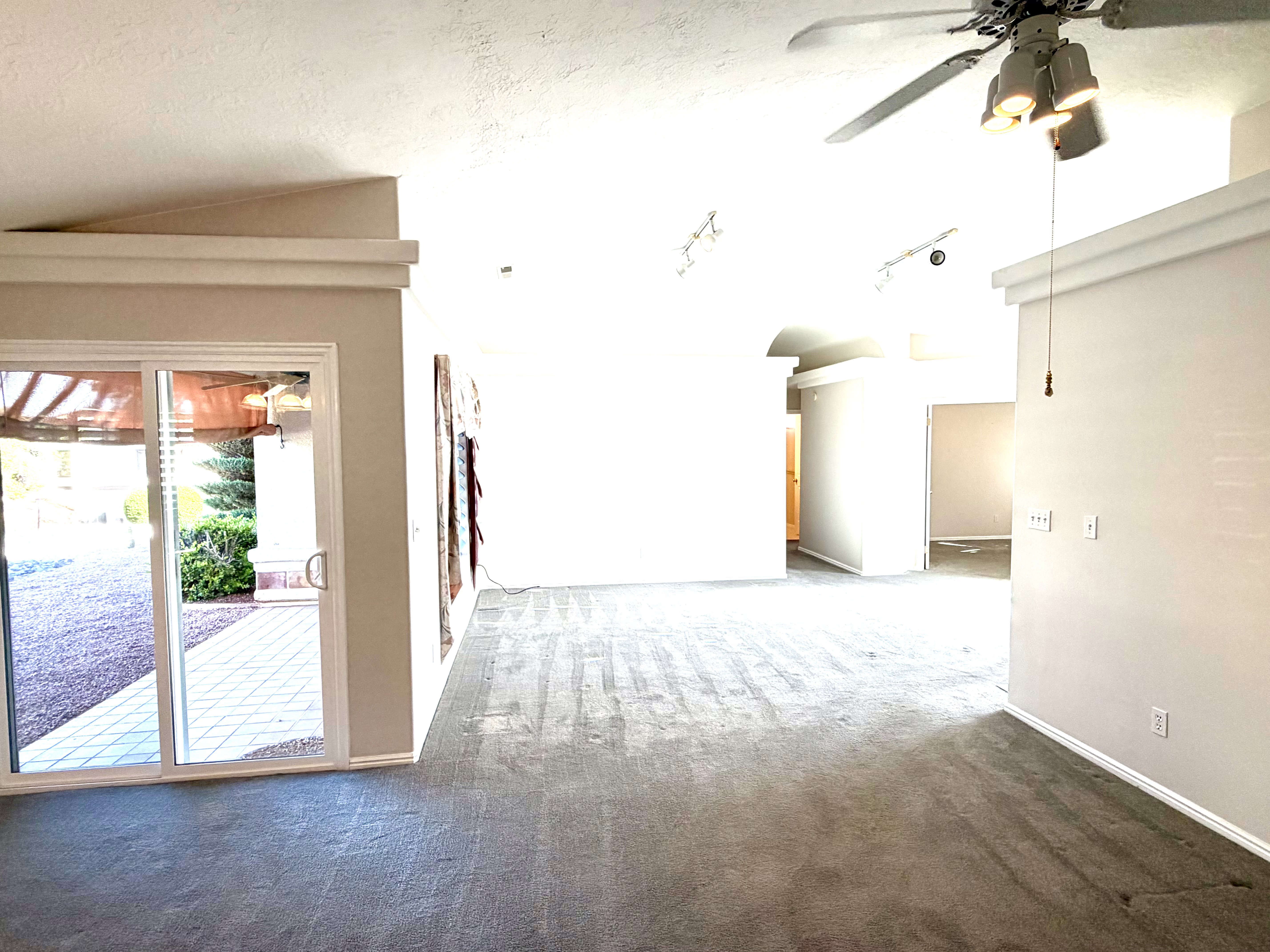 Spacious living area featuring neutral carpeting, a ceiling fan with integrated lighting, and vaulted ceilings