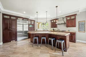 Kitchen with glass fronted cabinets, built in appliances, crown molding, a kitchen breakfast bar, and a kitchen island with sink