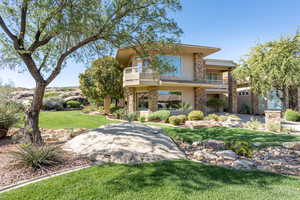 Rear view of house with a balcony, stucco siding, a yard, and stone siding