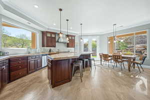 Kitchen with a center island, hanging light fixtures, backsplash, ornamental molding, and dishwasher