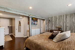 Bedroom with dark wood-type flooring, a closet, a textured ceiling, and wooden walls