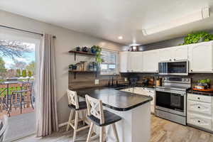 Kitchen featuring a peninsula, a breakfast bar, stainless steel appliances, white cabinets, and dark countertops