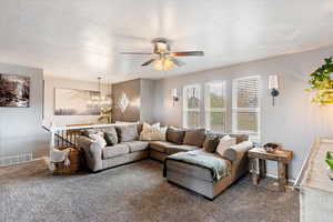 Living area with suspended lighting, a ceiling fan, dark colored carpet, and a textured ceiling