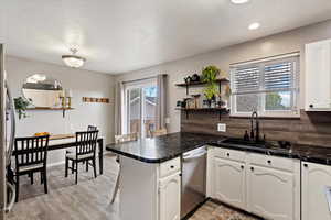 Kitchen with a peninsula, dark countertops, white cabinets, and a kitchen breakfast bar