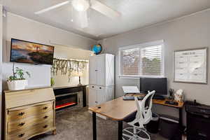 Office space featuring dark colored carpet, a ceiling fan, and a glass covered fireplace