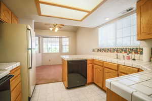 Kitchen featuring tile countertops, black appliances, wood finish cabinetry, and a peninsula