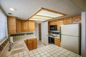 Kitchen with tile counters, white appliances, a textured ceiling, and wood finish cabinetry