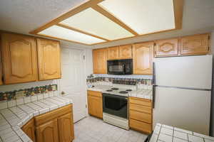 Kitchen featuring tile countertops, freestanding refrigerator, electric range, a textured ceiling, and black microwave
